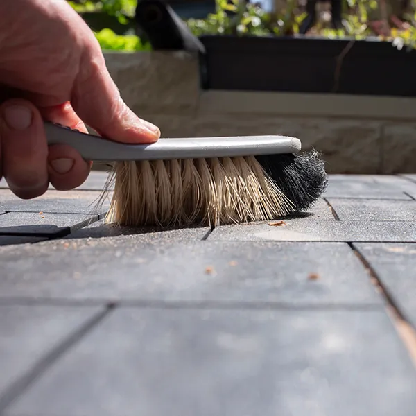 Person sweeping brick sidewalk with brush during spring cleaning.